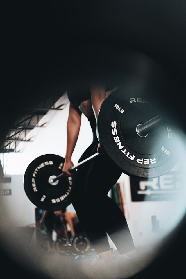 A woman in a dark, cold gym background lifting weights